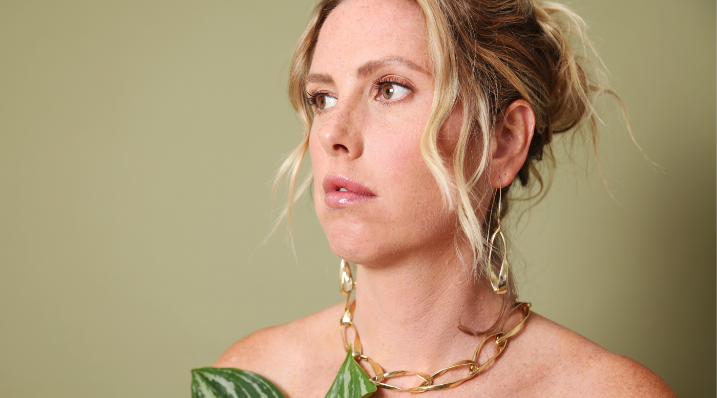 woman wearing bronze necklace and earrings against a green background