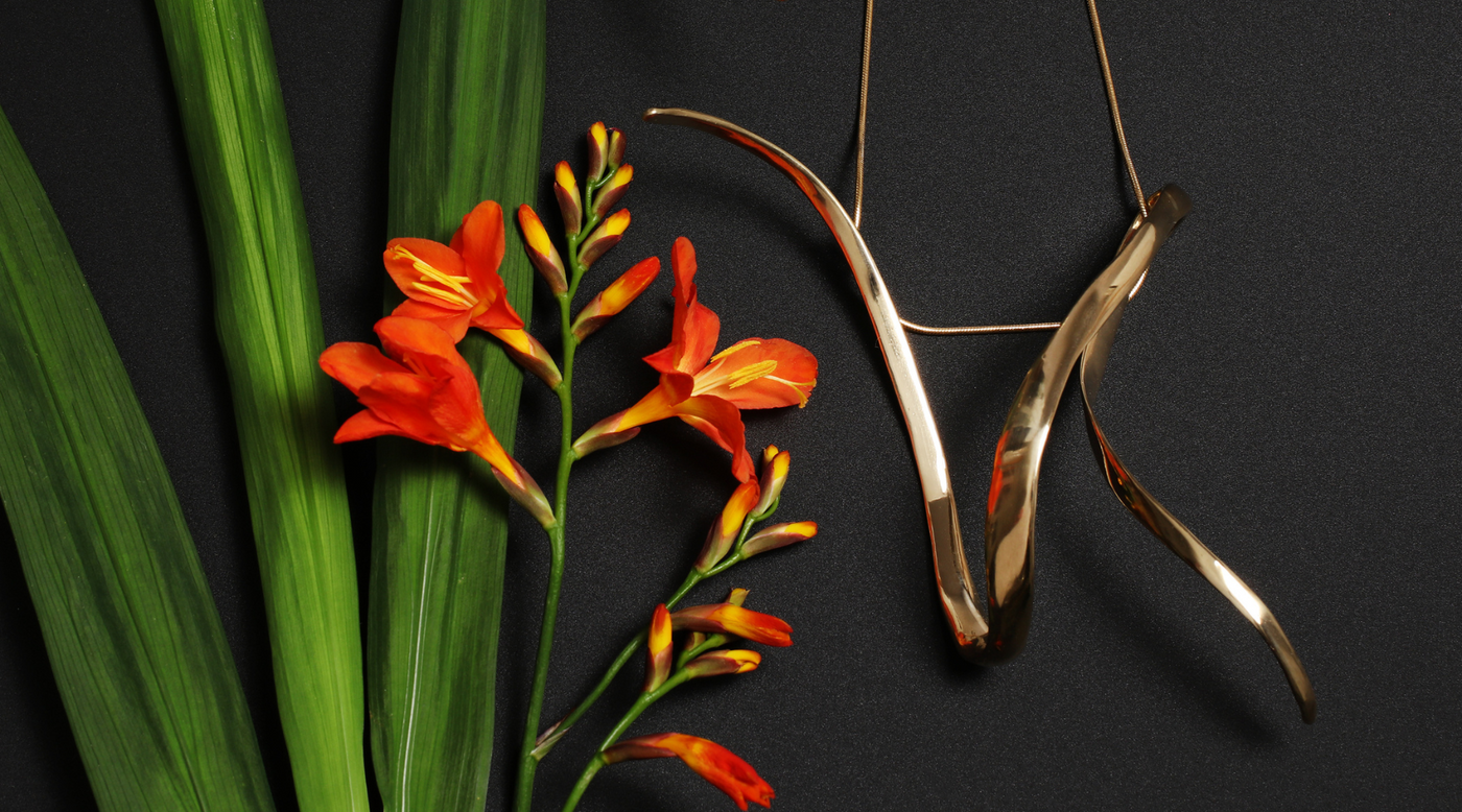 Unfurl bronze ribbon statement pendant necklace on black background with flowers